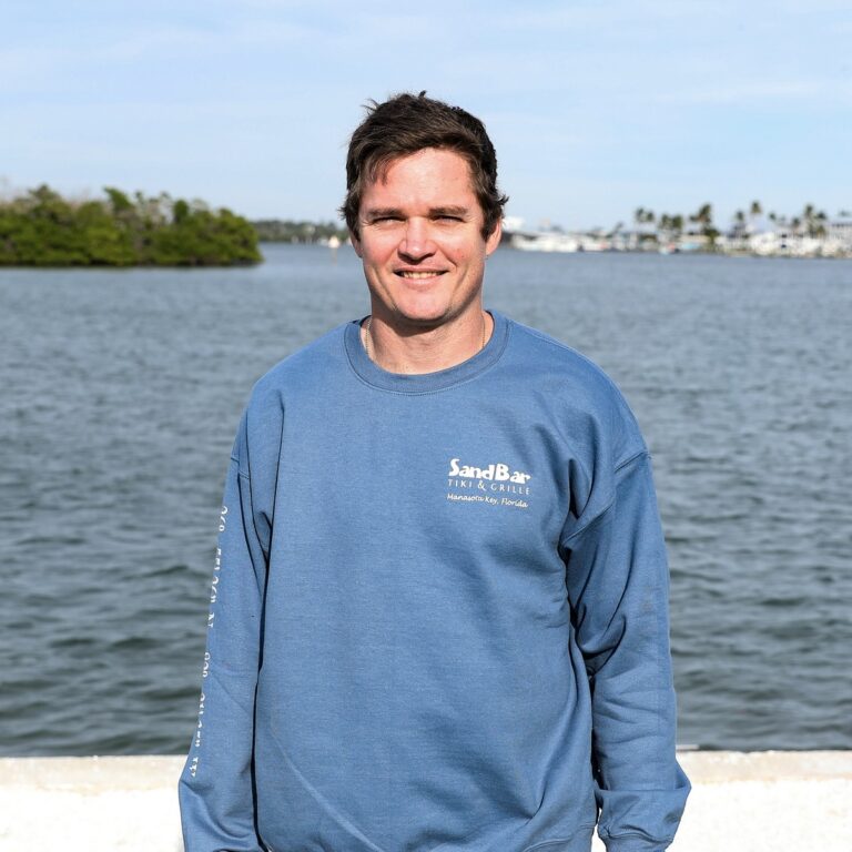 man wearing Sandbar Tiki & Grille Crewneck Sweatshirt with intracoastal waterway in the background